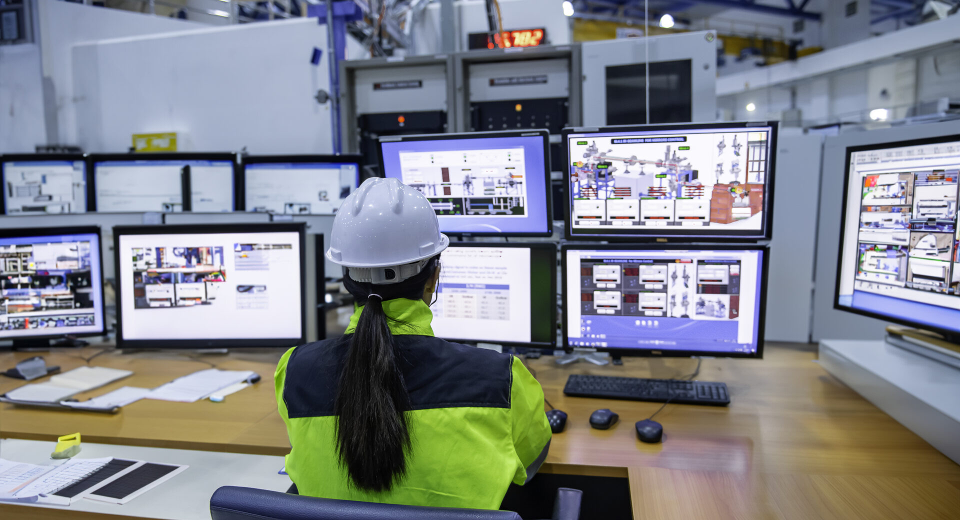 Mujer con casco trabajando en múltiples pantallas de ordenador en un entorno profesional.